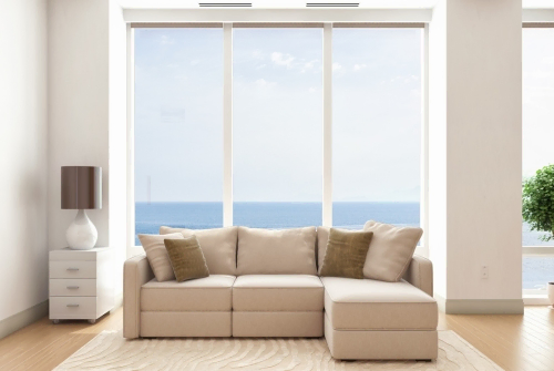 A neutral colored couch is situated by a window with the ocean in the background. This photo is for the blog post titled, "Timeless Home Decor Trends."